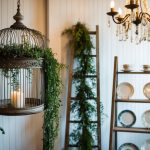 A vintage birdcage holds cascading greenery, while an old ladder serves as a display for antique plates and teacups. A chandelier made from repurposed candle holders adds a touch of elegance