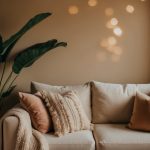 A cozy living room with soft, earthy tones, plush pillows, and warm lighting. A large, leafy plant sits in the corner, while a calming essential oil diffuser fills the air with a soothing scent